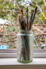 Various professional paint brushes in the transparent jar on the window sill