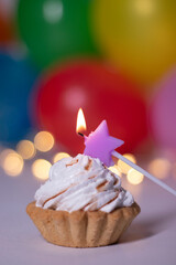 festive cupcake with a purple star-shaped candle. On the background of red gift box with a pink ribbon, multi-colored balloons and lights. party, birthday concept. Copy space. . High quality photo