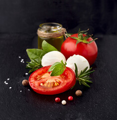 Fresh basil leaves with tomatoes, rosemary,oil and pepper on black stone background.