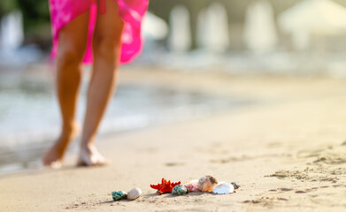 Closeup shells on sand, blurred of barefoot female young adult lower body relaxing in sea water on summer holiday. Sunset light. Travel concept. Copy space