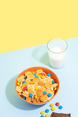 Orange bowl with tiny pancake cereal porridge with milk on a blue yellow background.Trendy tasty breakfast food