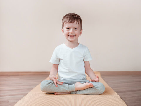 Kid meditates on a yoga Lotus position or Padmasana. Front view full length. Yoga exercises for kids at home
