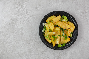 Roasted, baked potatoes on a black plate with fresh green onions and rosemary. Light gray background. Top view. Copy space.