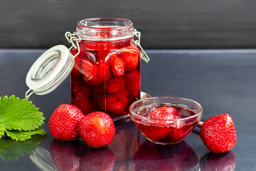 Strawberry jam in a glass jar next to fresh strawberries. On a black wooden background. Homemade winter fruit blanks. Selective focus.