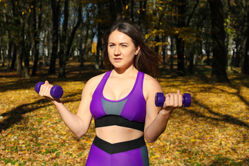 A girl in a bright tracksuit doing exercises with dumbbells in the park
