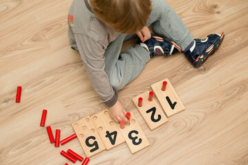 Baby sitting on the floor and inserting sticks in the right wooden cards with numbers. Educational calculate game teaching to develop. Intellectual kid math toy. Number Game Board.