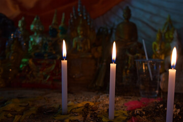 candles in the temple of Wat Sarmet in Thailand on Koh Samui, fire for offering to the deities, in the background are statues of Buddha and a glass of water as an offering to the saints