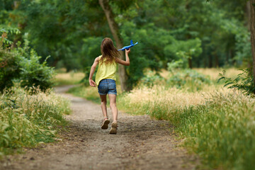 The concept of dreams and travel. Happy girl kid playing with toy airplane in summer on nature.