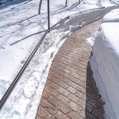 Square Stone brick pathway curving amid deep layer of fresh snow on a sunny winter day
