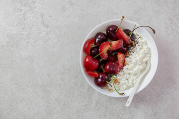 Cottage cheese with fresh cherry berries, plums, nuts and chia seeds. In a white bowl on a light background. Top view. Copy space.