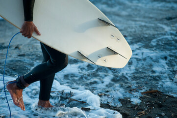 surfer man with surfboard in hand walking along the shore of the beach, surfboard on the beach at...
