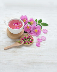 tea cup with hip roses on wooden white table. healthy vitamins tea with wild rose flowers and buds