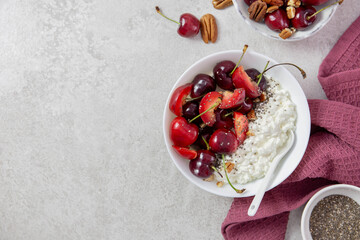Cottage cheese with fresh cherry berries, plums, nuts and chia seeds. In a white bowl on a light background. Top view. Copy space.