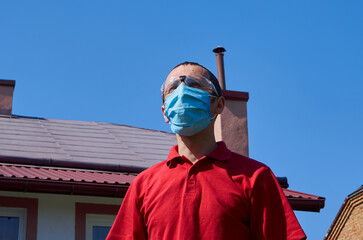 man in a mask on the background of the house,man standing in the yard of his house in a medical mask and glasses