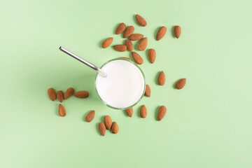 Almond milk in a glass with a straw, on a light green background, top view, almonds lie nearby.