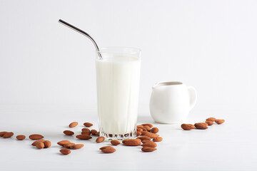 Almond milk in a glass goblet is on a white background, next to almonds and milkman. Healthy eating concept, horizontal orientation, close-up.