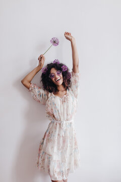 Slim girl with black wavy hair dancing at home and smiling. Chilling african young woman in romantic dress posing with flowers.