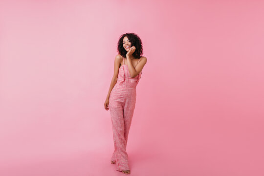 Gorgeous woman in wide pants posing with bare feet on pink background in cute studio