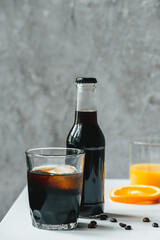 selective focus of cold brew coffee with ice in glass and bottle near orange juice and coffee beans on white table