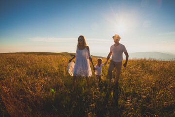 Sunny summer field with cheerful family walking through