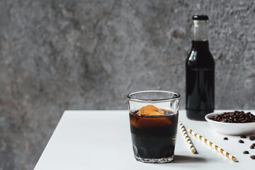 selective focus of cold brew coffee with ice in glass and bottle near drinking straws and coffee beans on white table