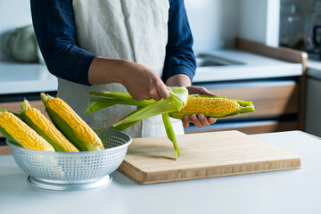 Man peeling corn husk at kitchen.