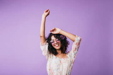 Indoor portrait of magnificent african woman standing on purple background with hands up. Studio shot of female model with wavy hair expressing good emotions.