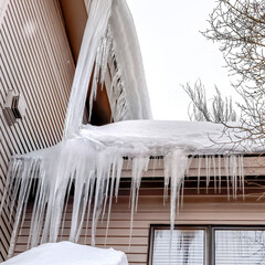 Square Roof of home with thick snow and sharp icicles against cloudy winter sky - obrazy, fototapety, plakaty