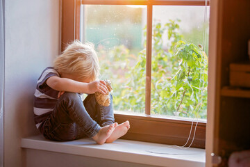 Abandoned little toddler boy, eating bread and sitting sad on a window shield