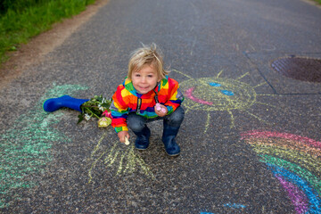 Cute toddler. playing in the rain with chalks, drawing on the asphalt, having fun