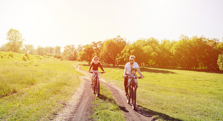 Happy family ride along sunlit fields. Man, woman and their baby on bikes.