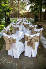 
Chairs with white covers are tied with large burlap bows for styling and atmosphere at the wedding, shot with a general plan frontally.