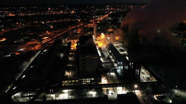 Top view of metallurgical plant blast furnace at night with smokestacks and fire blazing out of the pipe. Industrial panoramic landmark with blast furnance of metallurgical production