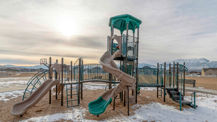 Panorama Slides on playground with remnants of snow on the ground against cloudy sky