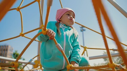 Cute little girl crawls in climbing net structure on playground holding at ropes - Powered by Adobe