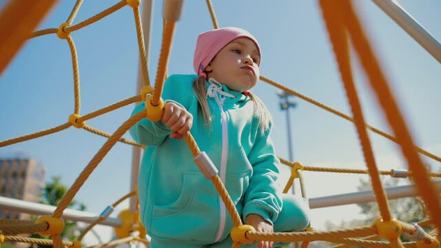 Cute little girl crawls in climbing net structure on playground holding at ropes
