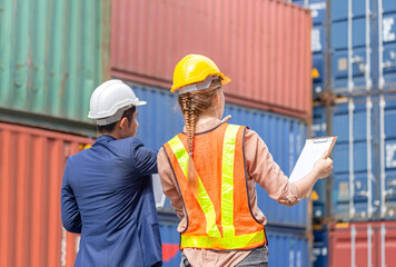 Engineer man in hardhat holding laptop and Female foreman worker holding clipboard checklist at containers cargo
