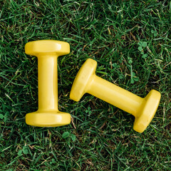 Set of two yellow dumbbells on a green grass background, top view. Staying in shape. Fitness and shape. Female exercise gear. Сoncept of outdoor fitness, nobody. Digital detox.