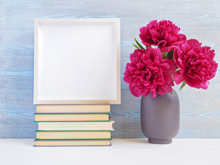 Flower composition. Layout with a bouquet of red peonies in a gray vase and an empty wooden photo frame. The composition is on a blue wooden background. Copy space.