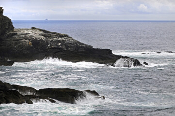 Vue panoramique sur les falaises de la pointe sud de l'Irlande. Mer, rochers, vagues et &eacute;cume sur fond d'eau turquoise et phare &agrave; l'horizon.