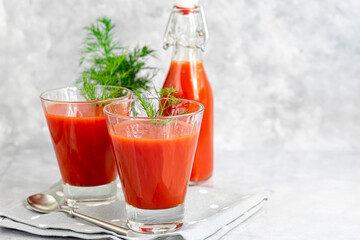 Tomato juice in glass cups and fresh tomatoes. On a light gray background. Vitamin drink. Garnished with sprigs of dill and coarse salt.