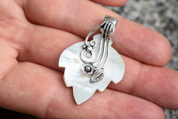 Natural white shell in the shape of leaf with silver decoration pendant on female hand