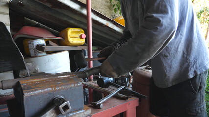 Fototapeta premium Unrecognizable man working with metal. Blacksmith processing iron detail using hammer. Mechanic or repairman working outdoors. Slow motion Close up