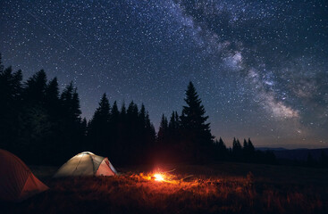 Burning bonfire in tent city without people under bright starry sky with Milky way against the...