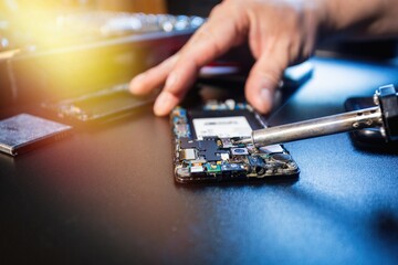 Technician repairing the smartphone's motherboard by soldering in the lab. Concept of computer...