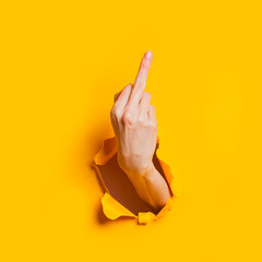 Female hand showing gesture meaning fuck you or fuck off through the hole in the yellow paper...