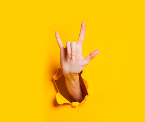 Female hand makes rock and roll gesture through hole in yellow paper.