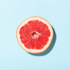 Top view on slice of grapefruit in sunlight on blue background. Minimal styled.