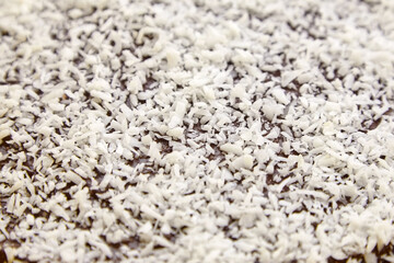 Chocolate cake decorated with flaked coconut, closeup. Homemade pie surface with coconut flakes, background