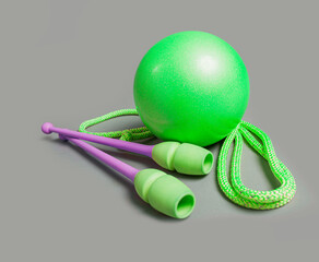 Professional equipment for gymnastics workout on grey background. Green ball, mace and rope for...